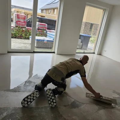 Vakman verdeelt egaline met een vlakspaan over de dekvloer van een lege woonkamer